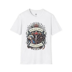 Puede incluir: Camiseta blanca con un estampado gráfico de una escena religiosa. El gráfico presenta una cruz con una figura sobre ella, una mujer de azul y un rosario. El texto "NEVER STOP PRAYING 1 THESSALONIANS 5:17" está impreso en el gráfico.