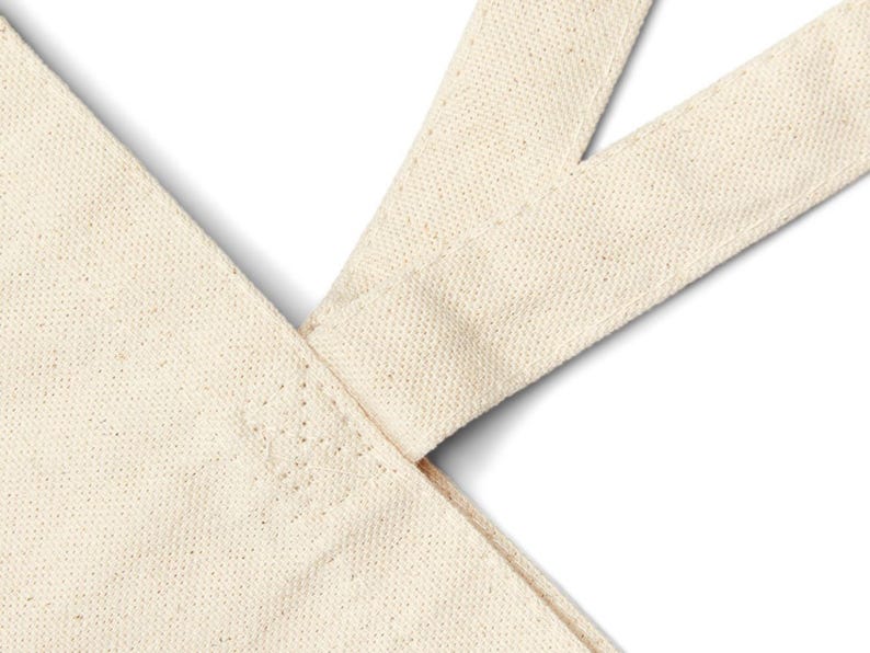 A blank, off-white canvas tote bag with reinforced handles for extra durability, the bag is made from durable cotton fabric in a natural, off-white color. The bag is spacious with a flat, sturdy bottom. Stitching from Chic Canvas Totes