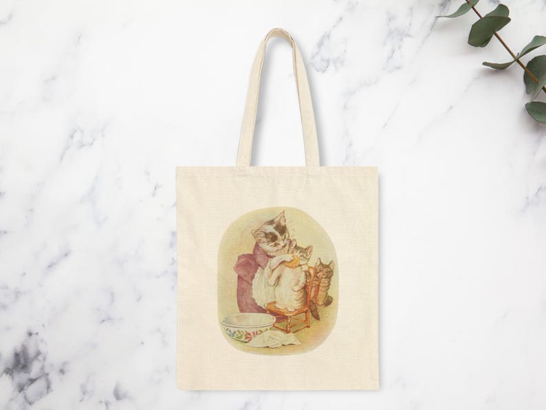 Mama Bag Tabitha Twitchit Tote Featuring Tom Kitten and Miss Moppet Cotton Canvas Tote Bag."Beatrix Potter Tabitha Twitchit Tote Bag featuring a vintage-style illustration of Tabitha Twitchit, the beloved mother cat from Tom Kitten’s story. Eco-friendly cotton tote with sturdy handles, perfect for book lovers, nursery decor, or everyday use. A charming gift for Beatrix Potter fans and collectors: front art image