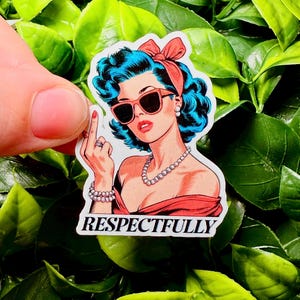 May include: A sticker featuring a retro illustration of a woman with blue hair, sunglasses, and a red bow. The woman is giving the middle finger. The word "RESPECTFULLY" is printed below the image.
