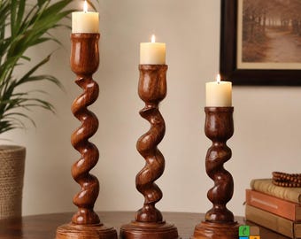 May include: Three dark brown wooden candle holders of varying heights, each featuring a spiraling, twisted stem design and a circular base. Each holder supports a single, lit, off-white pillar candle, creating a warm and vertical arrangement.