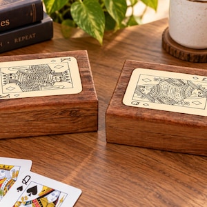 May include: Two rectangular wooden boxes with hinged lids, each featuring a light-colored inlay on top. One box displays a black line-art illustration of a King of Diamonds playing card, while the other shows a Queen of Diamonds playing card.