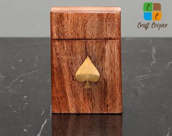 May include: A rectangular wooden box with a hinged lid, featuring a prominent brass spade symbol inlaid on the front face. The wood displays a natural brown grain pattern. The text Craft Cooper is visible in the upper right corner of the image.