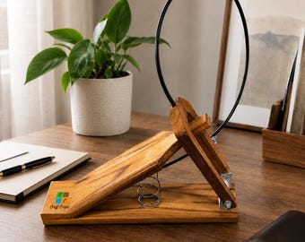 May include: A wooden book stand with a slanted base, a spring mechanism, and a black circular wire frame. The wood features a natural grain, and the base is marked with a colorful square logo and the text Craft Coope in black lettering.