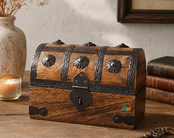 May include: A rectangular wooden chest with a domed lid, featuring dark metal bands, decorative circular studs, and a central heart-shaped latch. The wood has a visible grain, and the metal hardware is finished in a dark, weathered tone.