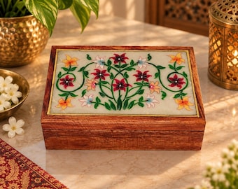 May include: A rectangular wooden box featuring a white stone inlay on the lid. The inlay displays a symmetrical floral pattern with green vines and flowers in shades of red, pink, and yellow. The box has a natural wood grain finish.