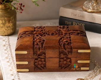 May include: A rectangular wooden box with a dark brown finish, featuring intricate floral carvings on the lid and front panel. The box is accented with smooth, polished brass corner plates on the front edges and includes a small logo with the text Craft Cooper.