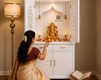 May include: A white wooden home temple cabinet featuring two doors with intricate cut-out patterns, a central shelf holding a gold-toned Ganesha statue, two hanging brass bells, and two small brass oil lamps. The cabinet includes two drawers.
