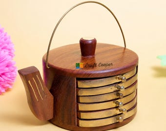 May include: A wooden teapot-shaped holder with a metal handle and a lid, containing a stack of six circular brass coasters. The dark brown wood features a carved spout and the text Craft Cooper printed on the lid, providing a storage solution.