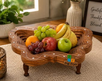 May include: A collapsible wooden fruit bowl with a natural brown finish and white painted accents, featuring a multi-layered design on four short legs. The bowl is filled with fresh fruit including green grapes, a red apple, a green apple, and bananas.