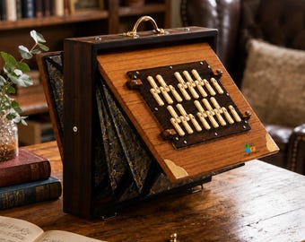 May include: A wooden accordion-style musical instrument with a dark brown finish, featuring a brass handle and corner accents. The front panel displays a grid of ivory-colored keys mounted on a dark wood base, with marbled bellows visible on the side.