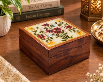 May include: A square wooden box with a dark brown finish and a hinged lid. The top of the lid features an inlaid white stone panel decorated with a colorful floral pattern of red, yellow, and light blue flowers with green stems and leaves.