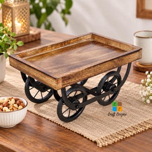 May include: A rectangular wooden tray with a natural brown wood grain finish, mounted on a black metal frame featuring four circular wheels. The tray has raised edges and is supported by curved metal supports connecting the wheels to the base.