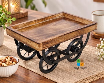 May include: A rectangular wooden tray with a natural brown wood grain finish, mounted on a black metal frame featuring four circular wheels. The tray has raised edges and is supported by curved metal supports connecting the wheels to the base.