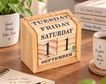 May include: A wooden perpetual desk calendar featuring rotating blocks for the day of the week, the date, and the month. The light-colored wood frame holds blocks printed with black text, currently displaying Tuesday, Friday, Saturday, 11, and September.