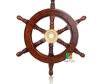 May include: A dark brown wooden ship wheel featuring six spokes and a central circular brass hub. The wheel has a polished finish and a smooth texture. A small logo with the text Craft Cooper is visible in the lower right quadrant of the wheel.