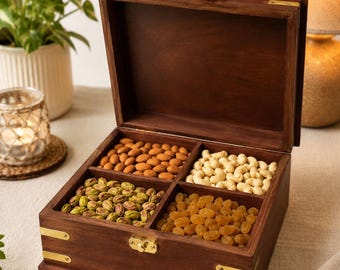 May include: A square dark brown wooden storage box with a hinged lid and gold-toned metal latches and corner accents. The interior is divided into four equal compartments filled with almonds, cashews, pistachios, and raisins. The text Craft Cooper is visible.