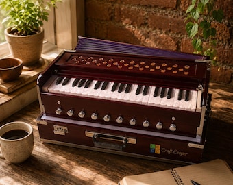 May include: A dark wood harmonium musical instrument featuring a keyboard with white and black keys, a row of silver knobs, and a purple bellows section. The front of the instrument displays the text Craft Cooper with a colorful square logo.