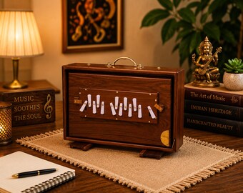 May include: A rectangular wooden harmonium instrument featuring a dark brown wood grain finish, a brass handle on top, and a central panel with white keys. The instrument is supported by two small wooden feet and includes brass corner accents.
