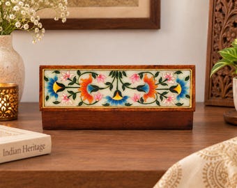May include: A rectangular wooden box featuring a central white stone inlay panel decorated with a colorful floral pattern. The design includes orange, blue, and pink flowers with green stems and leaves, framed by a thin gold-colored border.