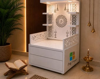 May include: A white wooden home temple featuring a central Om symbol, intricate laser-cut patterns, two storage drawers, and integrated lighting. The structure includes side shelves, hanging metal bells, and a smooth top surface for placement.