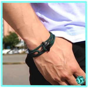 Könnte beinhalten: Ein dunkelgrünes Seil-Armband mit einem schwarzen Anker-Anhänger.