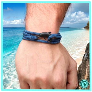 Op de afbeelding: Een blauwe touw armband met een zwarte dolfijn bedel. De armband wordt gedragen op een pols.