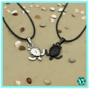 Op de afbeelding: Twee kettingen met schildpad hangers. Een hanger is zilver en de andere is zwart.