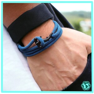 Peut inclure: Un bracelet en corde bleu avec un fermoir d'ancre noir. Le bracelet est porté au poignet.