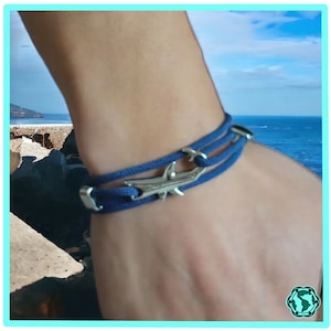 Pode incluir: Uma pulseira trançada azul com um fecho de tubarão prateado. A pulseira é usada no pulso.
