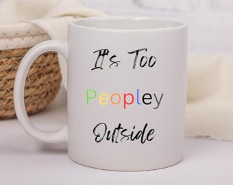 May include: White ceramic coffee mug with the text "It's Too Peopley Outside" in black. The word "Peopley" is written in rainbow colors.