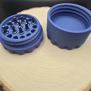 Puede incluir: Un contenedor de almacenamiento redondo y azul de varios compartimentos con tapa. El contenedor está lleno de pequeñas herramientas plateadas.