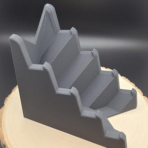 May include: A gray plastic display stand with five tiers, designed to hold small items like jewelry or figurines.