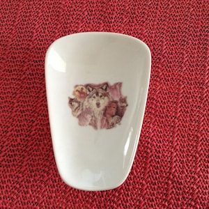 May include: White ceramic spoon rest with a colorful image of wolves printed on the front.