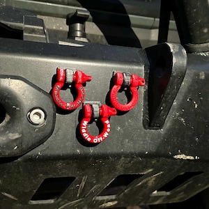 May include: Three red metal tow hooks with the text "Middle Off-Road" printed on one of them. The hooks are attached to a black metal bumper.