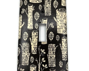 May include: A rectangular light switch plate cover featuring a black background with a repeating pattern of cream-colored tree trunks and leaves. The design is overlaid with black printed text in a serif font, creating a layered visual effect.
