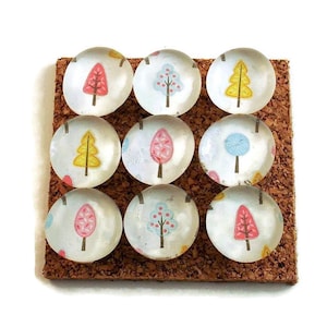 May include: Set of 10 clear glass push pins with colorful tree designs. The trees are pink, yellow, blue, and green. The push pins are on a cork board.