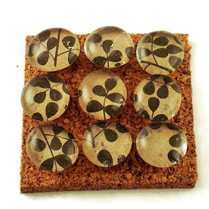 May include: Nine glass push pins with a black and gold leaf pattern on a cork board.