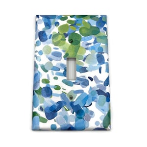 May include: A decorative light switch cover featuring a watercolor design. The cover has a white background with blue and green abstract shapes. The switch opening is a vertical rectangle.