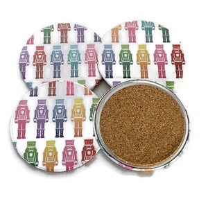 May include: Set of four round coasters with a white background and a repeating pattern of colorful nutcracker figures. One coaster is flipped over, revealing a cork base. The nutcrackers are in various colors, including red, blue, and green.