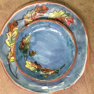 May include: A set of two blue ceramic plates with a hand-painted design of autumn leaves in shades of yellow, orange, and red. The plates are nested together.