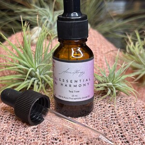 May include: A small amber glass bottle with a black dropper lid. The bottle is labeled "Essential Harmony Tea Tree 15 ml 100% Pure Therapeutic Grade Oil".