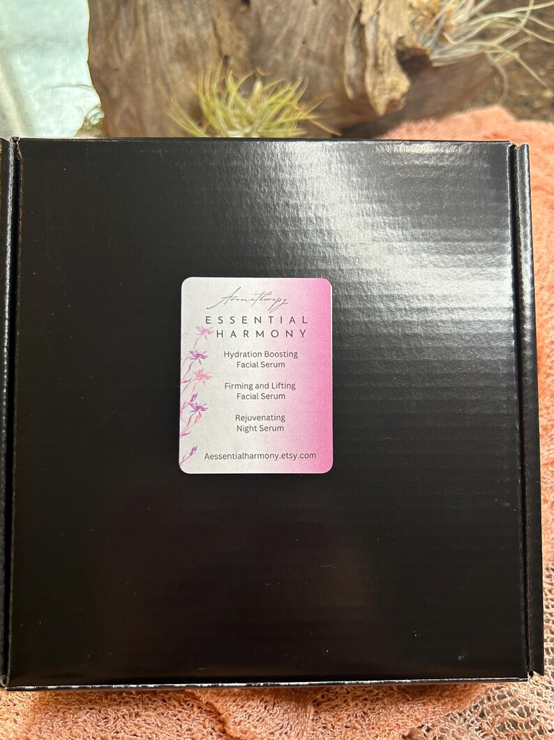 May include: A black box with a pink and white label. The label reads "ESSENTIAL HARMONY" and lists facial serums: Hydration Boosting, Firming and Lifting, and Rejuvenating Night Serum. The website Aessentialharmony.etsy.com is also listed.