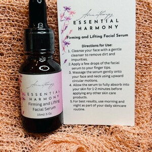 May include: A brown glass bottle with a black dropper and a label that reads "ESSENTIAL HARMONY Firming and Lifting Facial Serum 15ml/.5 Oz." A white card next to it provides usage directions. The background is a peach-colored, textured fabric.