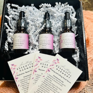 May include: A skincare gift set featuring three glass dropper bottles of facial serum, each labeled with "Essential Harmony." The set includes cards with instructions. The bottles are in a black box with white paper filler.
