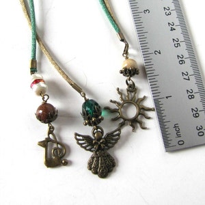 May include: A green and beige cord necklace with a variety of charms, including a sun, an angel, a musical note, and several beads. The necklace is approximately 29 inches long.