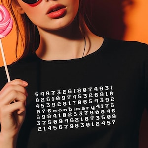 Könnte beinhalten: Eine Frau trägt ein schwarzes T-Shirt mit weißem Text, der "549732618074931 826109745326810 453928170654392 076nonbinary4176 698410253790846 375094621873509 214567983012457" lautet.