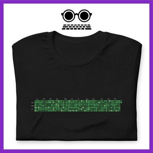Może przedstawiać: Czarny T-shirt z zieloną, pikselową grafiką kalendarza. Kalendarz pokazuje miesiące roku, od stycznia do grudnia.