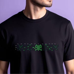 以下が含まれることがあります： 緑色のピクセルでできたカレンダーのデザインが施された黒いTシャツ。カレンダーには、年の月と曜日が表示されています。