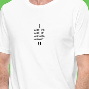 Puede incluir: Camiseta blanca con un diseño gráfico negro que dice "I 01101100 01101111 01110110 01110010 01100101 U".